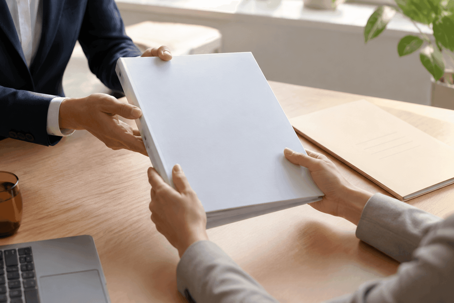Two people hand a bound, unbranded report across a desk to one another